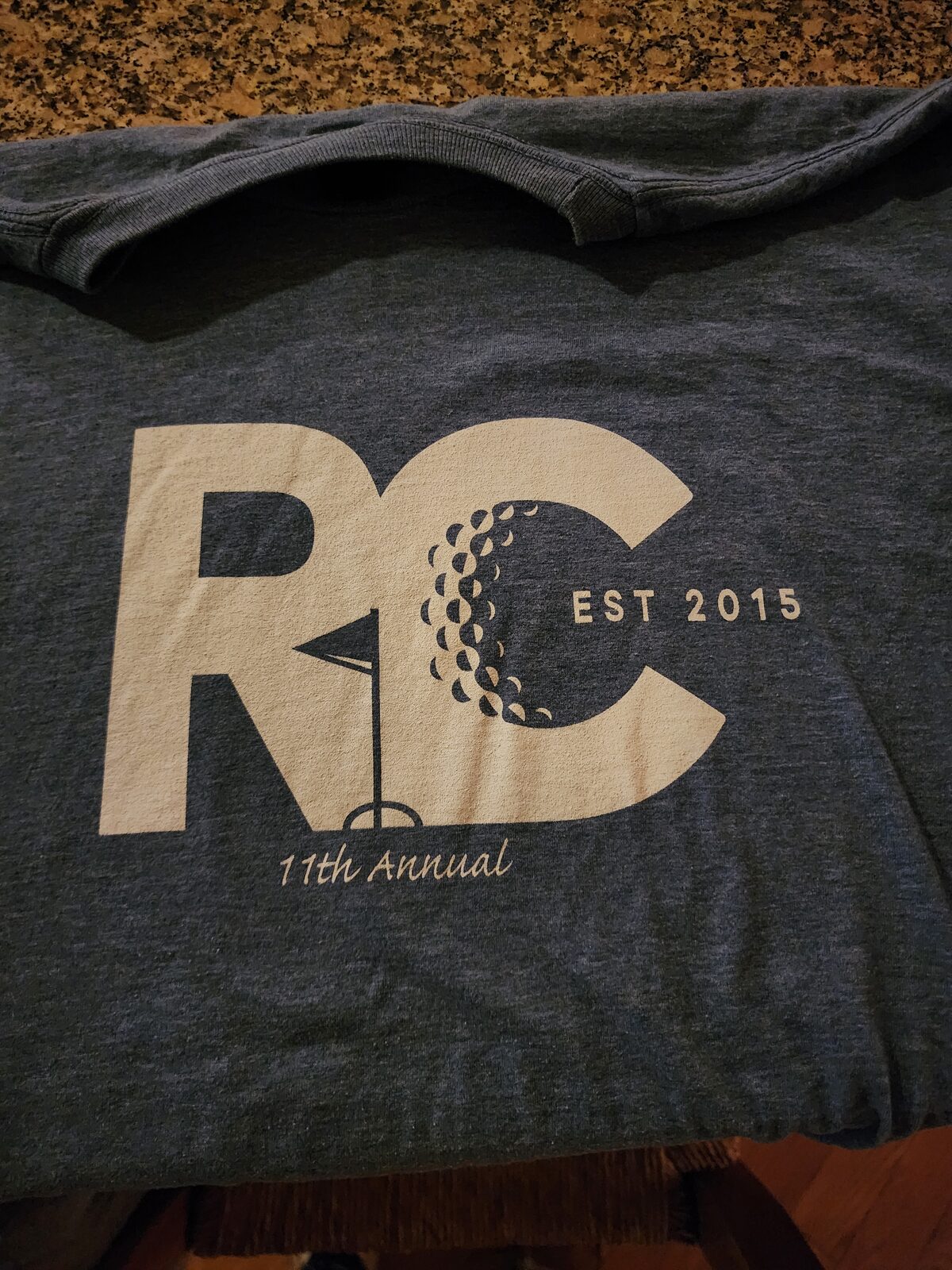The RC11 shirt: a cream RC monogram with a golf ball in the C and a flag in the R, Est. 2015